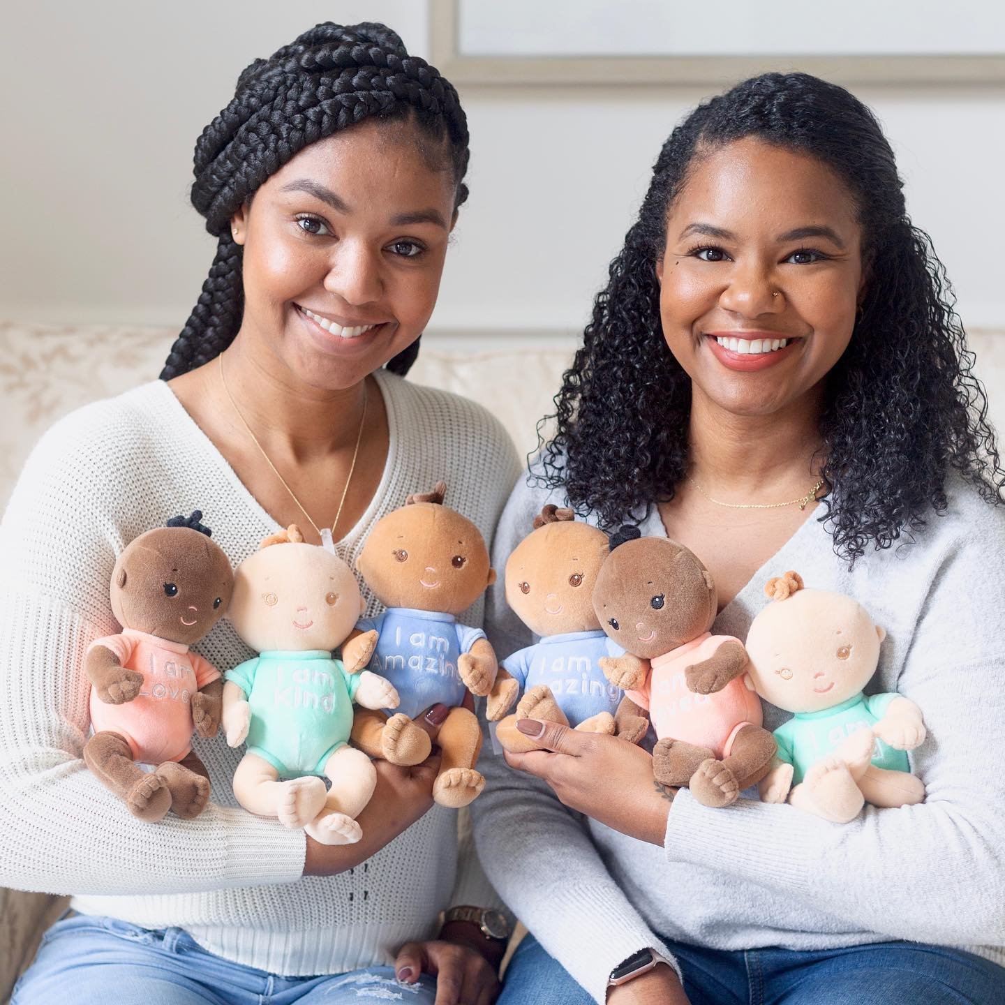 two women holding soft dolls with varying skin tones